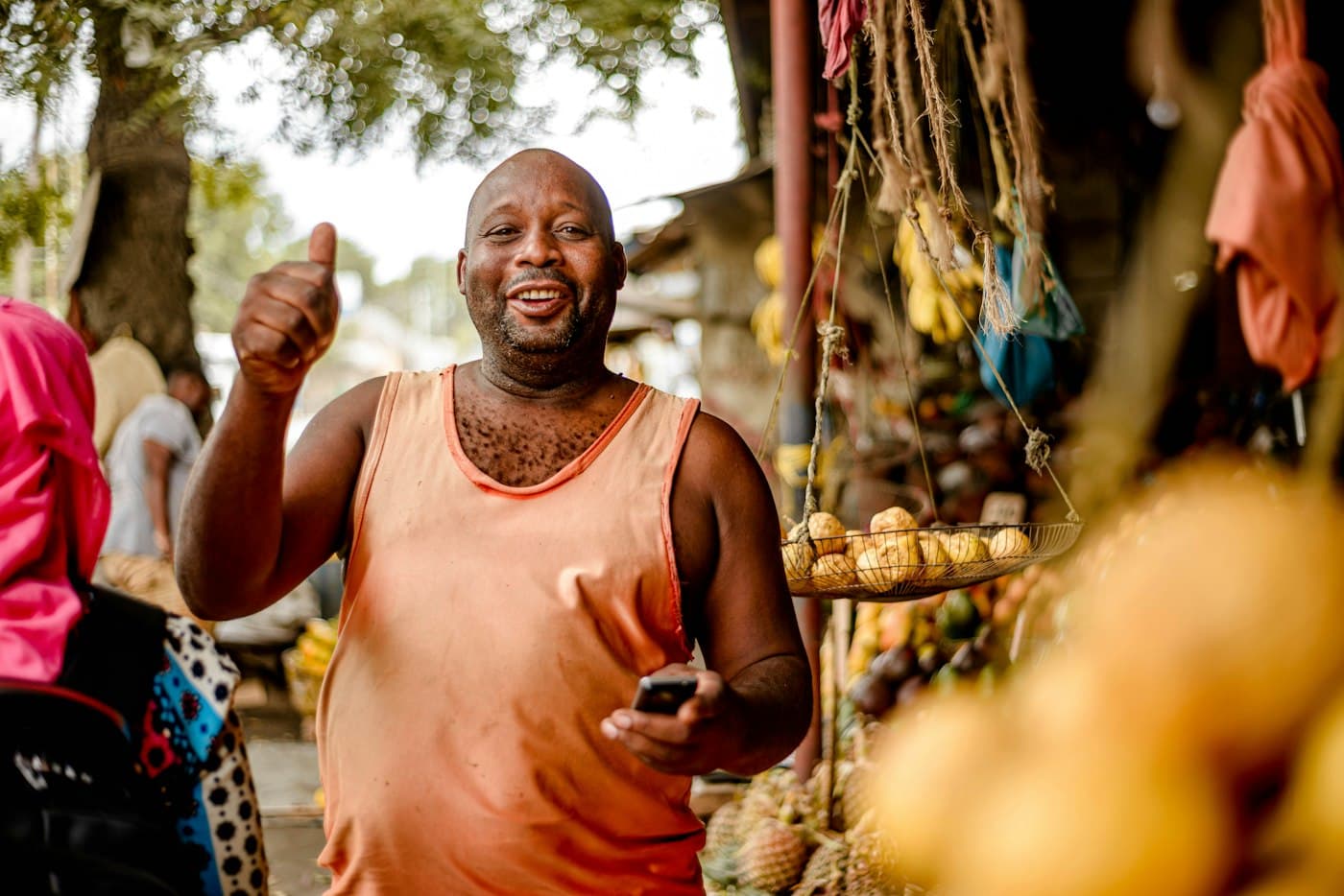 A stallholder gives a thumbs up at his market stand, holding a phone