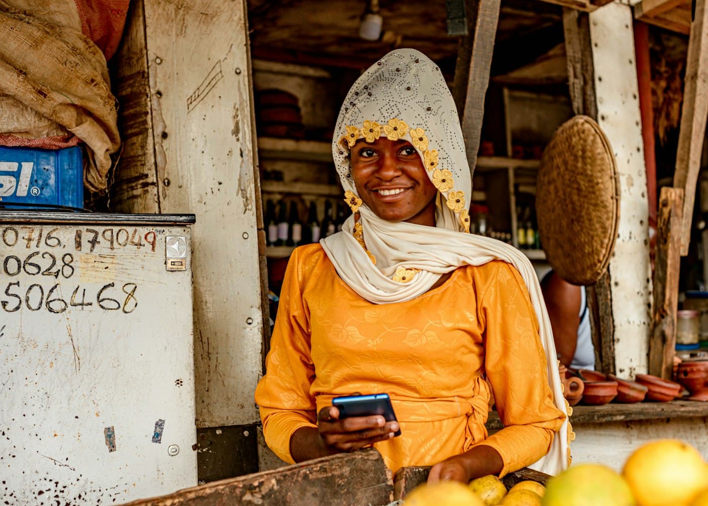 A market trader smiles at her fruit stall, phone in hand